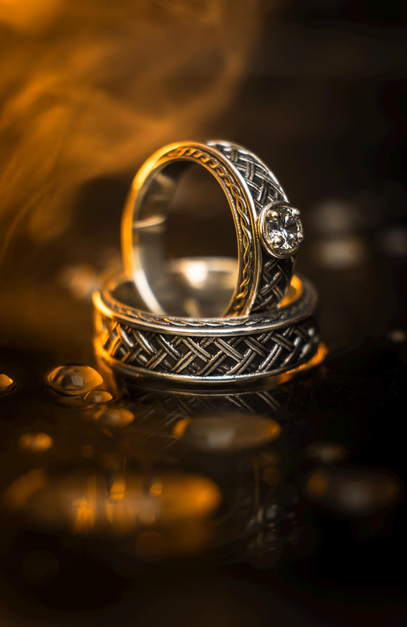 A cinematic studio shot of a wide sterling silver ring lying on a reflective golden surface. The band features a central "basket weave" pattern—diagonal strands of silver crossing over and under each other. The edges are framed by a distinct "rope" or "cable" twist border. The raised metal is polished silver, while the deep recesses are blackened to highlight the intricate weaving.