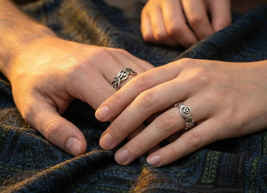 A cinematic macro shot of a sterling silver ring bathed in warm, golden light. The focal point is the central oval face, which encloses a raised relief design of two spirals meeting in the center to suggest a heart shape. The band shoulders feature textured knotwork that leads up to the centerpiece. The ring rests on a wet, reflective surface, creating a mirror image of the love knot below. (etsy image id: 7490345549)