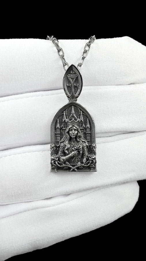 A close-up studio shot of a sterling silver pendant shaped like a Gothic cathedral arch. In the center, a sculpted queen or goddess with long flowing hair and a pointed crown holds a single rose to her chest. Behind her are intricately detailed cathedral spires. The bottom is framed by intertwined rose stems and blooms. The dark oxidation perfectly highlights the bright polished silver relief. __etsy:8051007659