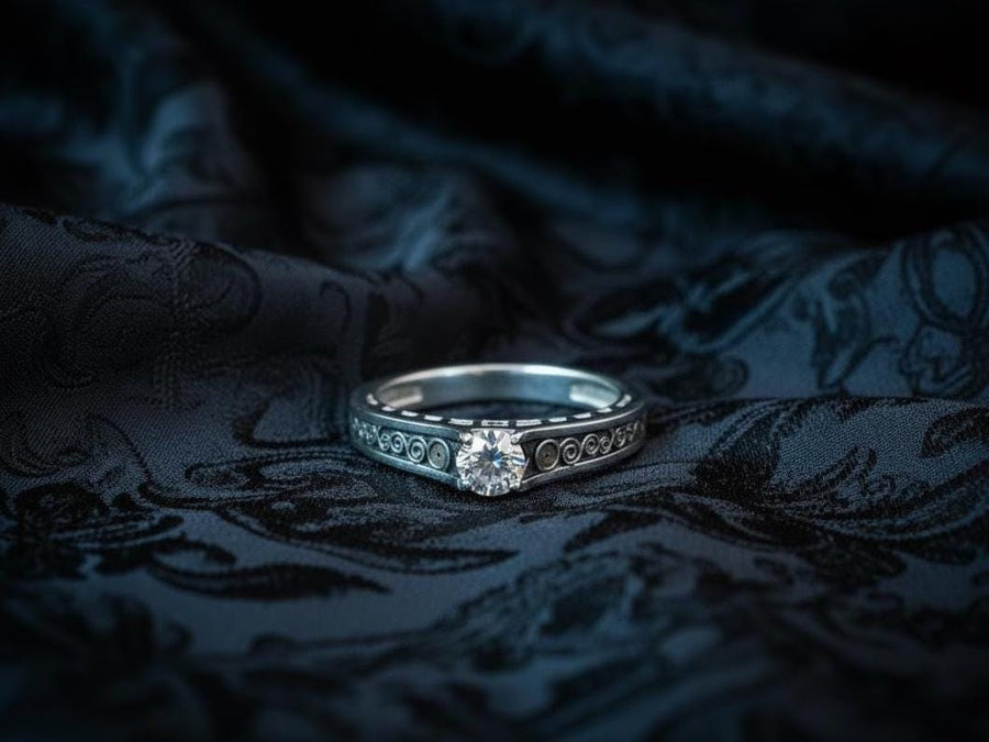 A detailed macro shot of a sterling silver engagement ring. The focal point is a round, honey-colored gemstone (Citrine or Madeira Topaz) set flush into the band. The shank is decorated with a continuous relief pattern of spirals and circles, mimicking the decorative robes found in Gustav Klimt's "Golden Phase" paintings. The silver features an oxidized finish, creating a dark background that makes the polished spirals pop. (etsy image id: 7142785932)