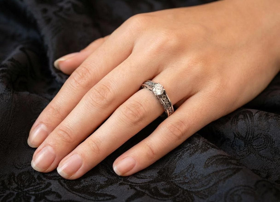 A detailed macro shot of a sterling silver engagement ring. The focal point is a round, honey-colored gemstone (Citrine or Madeira Topaz) set flush into the band. The shank is decorated with a continuous relief pattern of spirals and circles, mimicking the decorative robes found in Gustav Klimt's "Golden Phase" paintings. The silver features an oxidized finish, creating a dark background that makes the polished spirals pop. (etsy image id: 7142785932)