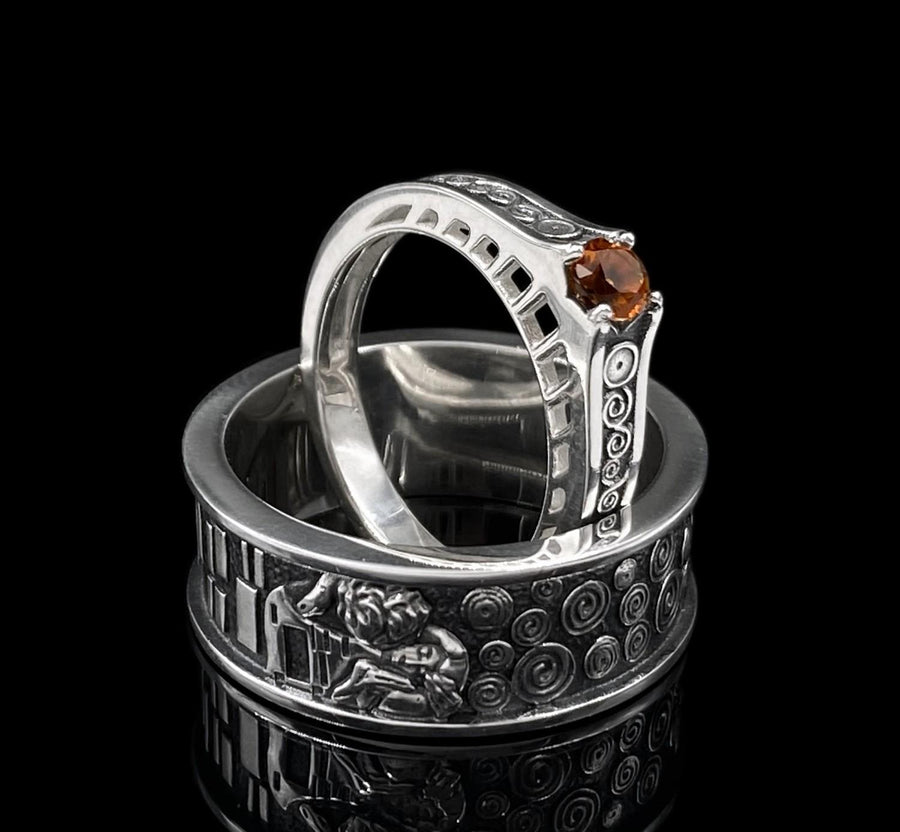A detailed profile shot of a wide sterling silver ring standing on a reflective surface. The band features a raised relief carving of the figures from Gustav Klimt's painting "The Kiss." To the left of the couple are sharp, vertical rectangular blocks. To the right are swirling circular spirals. The background of the carving is darkened with oxidation to contrast with the polished silver figures. __etsy:7442609320