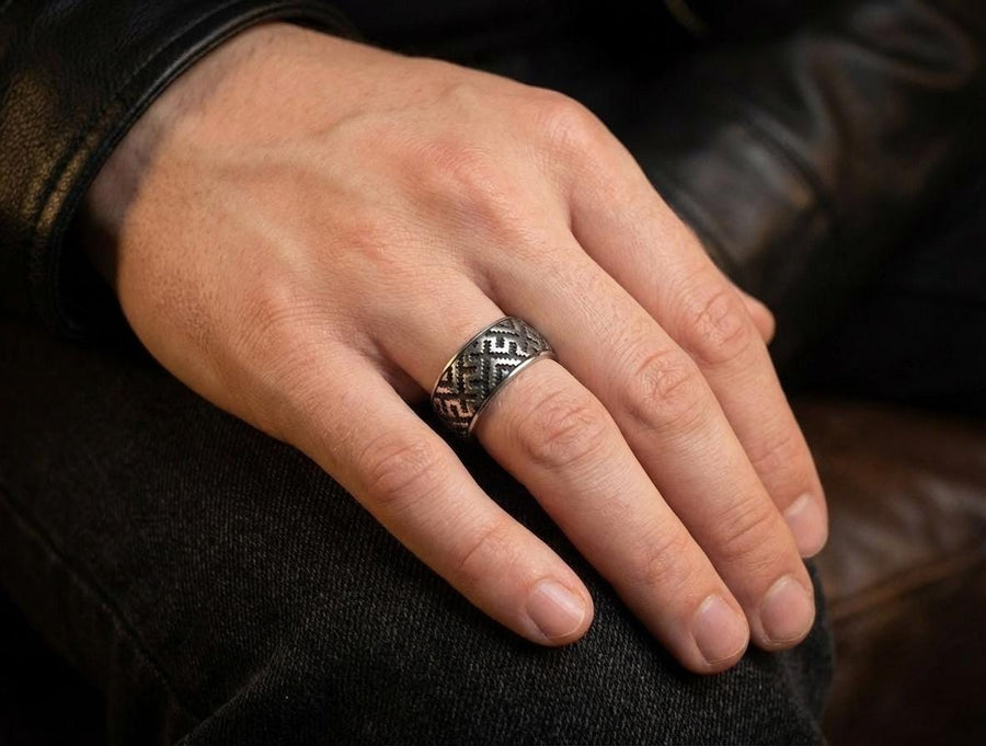 A detailed profile shot of a wide sterling silver ring featuring a repeating "step" or "zig-zag" pattern. The design wraps seamlessly around the entire band. The raised geometric lines are highly polished, catching the light, while the recessed areas are treated with a matte black oxidation. This creates a high-contrast, graphic look similar to a digital pixel pattern or traditional cross-stitch embroidery. (etsy image id: 7438608638)