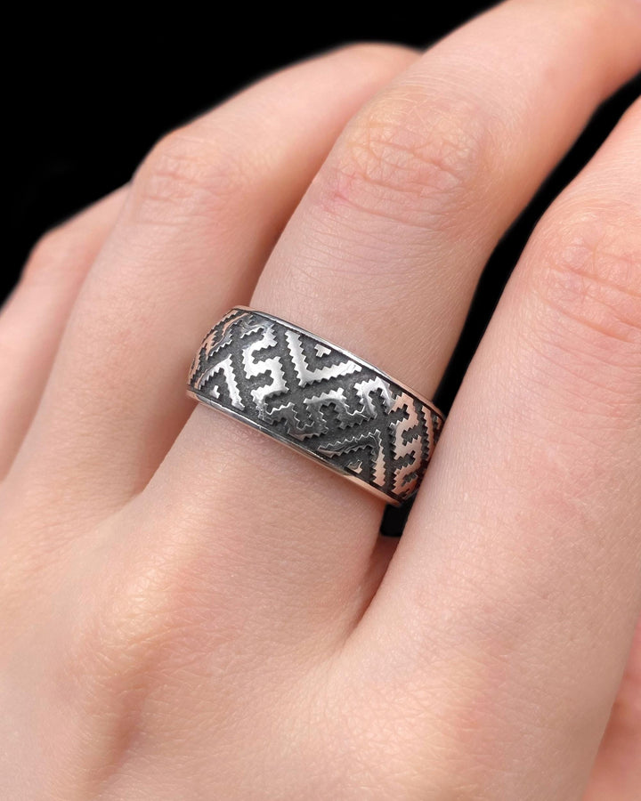 A detailed profile shot of a wide sterling silver ring featuring a repeating "step" or "zig-zag" pattern. The design wraps seamlessly around the entire band. The raised geometric lines are highly polished, catching the light, while the recessed areas are treated with a matte black oxidation. This creates a high-contrast, graphic look similar to a digital pixel pattern or traditional cross-stitch embroidery. (etsy image id: 7438608638)