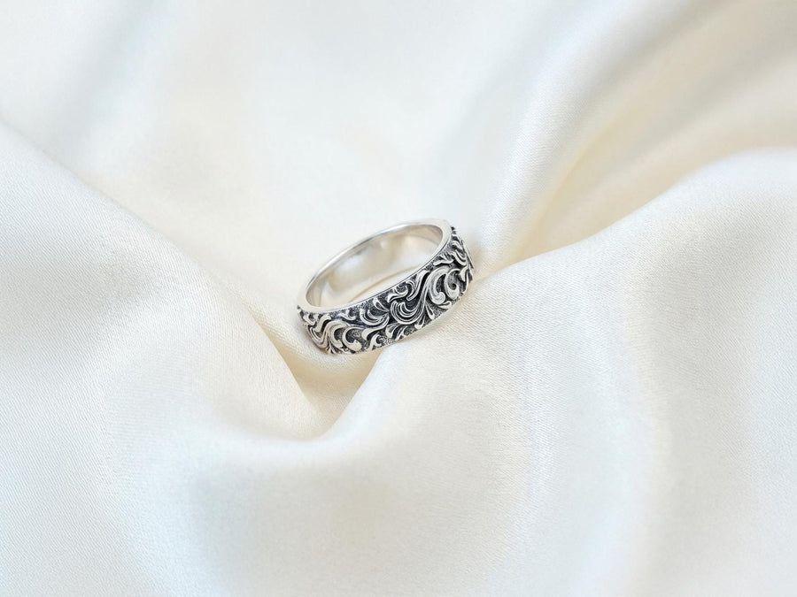 A close-up studio shot of a matching organic gothic wedding band set in sterling silver, resting on a dark, reflective surface. The rings feature a continuous, high-relief pattern of intricate sterling silver vine patterns and swirling leaves. The recessed areas are heavily oxidized to a dark matte black, creating a high-contrast shadow effect that makes the polished organic scrollwork stand out brilliantly against the dark background. __etsy:8017806924
