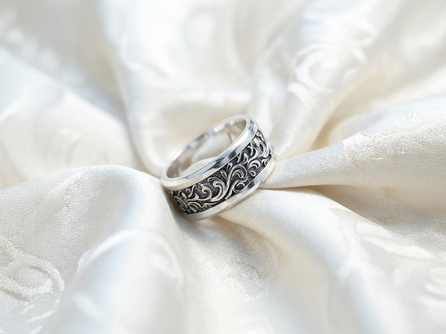 A close-up studio shot of a matching organic gothic wedding band set in sterling silver, resting on a dark, reflective surface. The rings feature a continuous, high-relief pattern of intricate sterling silver vine patterns and swirling leaves. The recessed areas are heavily oxidized to a dark matte black, creating a high-contrast shadow effect that makes the polished organic scrollwork stand out brilliantly against the dark background. __etsy:8017806924