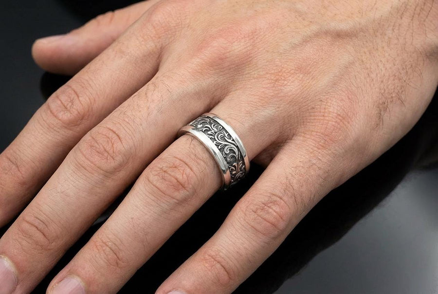 A close-up studio shot of a matching organic gothic wedding band set in sterling silver, resting on a dark, reflective surface. The rings feature a continuous, high-relief pattern of intricate sterling silver vine patterns and swirling leaves. The recessed areas are heavily oxidized to a dark matte black, creating a high-contrast shadow effect that makes the polished organic scrollwork stand out brilliantly against the dark background. __etsy:8017806924