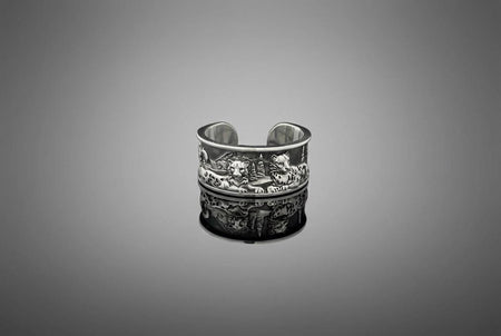 A close-up studio shot of a wide, open-back sterling silver cuff ring resting on a black reflective surface. The band features a detailed, three-dimensional bas-relief carving of a mountain landscape. In the foreground, two realistic snow leopards lie side by side among textured pine trees and rocky peaks. The 925 silver is heavily oxidized in the recesses to highlight the intricate fur spots, trees, and mountainous terrain against the polished r __etsy:7979063548