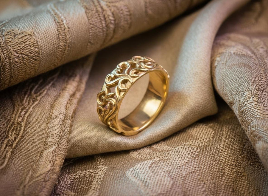 A detailed close-up of a wide sterling silver ring resting on a reflective surface. The band is covered in a deep-relief filigree pattern consisting of interlocking scrolls, vines, and subtle heart shapes. The raised designs are polished bright silver, while the recessed background is heavily oxidized to black, highlighting the complexity of the Baroque motif.