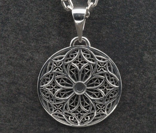 A detailed studio shot of a circular sterling silver pendant resting on a dark, textured slate background. The design is a geometric lattice based on the number four (quatrefoil). Four large teardrop-shaped arches meet in the center, subdivided by finer tracery lines. The raised silver network is polished, contrasting with the matte black oxidation in the negative spaces. __etsy:7446488454