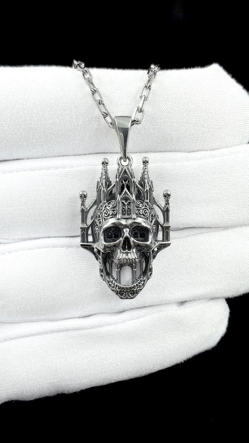 A close-up studio photograph of a highly detailed sterling silver pendant hanging from a sturdy chain against a black background. The striking design seamlessly merges the lower half of a fanged human skull with the upper structure of a Gothic cathedral. The architecture features soaring spires, pointed lancet arches, and intricate openwork tracery, with tiny skulls resting atop the outer pillars. __etsy:8027326873