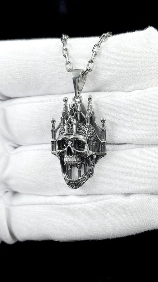 A close-up studio photograph of a highly detailed sterling silver pendant hanging from a sturdy chain against a black background. The striking design seamlessly merges the lower half of a fanged human skull with the upper structure of a Gothic cathedral. The architecture features soaring spires, pointed lancet arches, and intricate openwork tracery, with tiny skulls resting atop the outer pillars. __etsy:8027326873