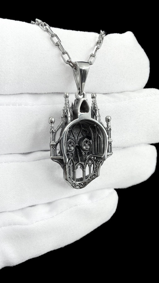 A close-up studio photograph of a highly detailed sterling silver pendant hanging from a sturdy chain against a black background. The striking design seamlessly merges the lower half of a fanged human skull with the upper structure of a Gothic cathedral. The architecture features soaring spires, pointed lancet arches, and intricate openwork tracery, with tiny skulls resting atop the outer pillars. __etsy:8027326873