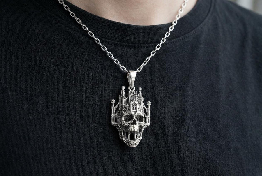 A close-up studio photograph of a highly detailed sterling silver pendant hanging from a sturdy chain against a black background. The striking design seamlessly merges the lower half of a fanged human skull with the upper structure of a Gothic cathedral. The architecture features soaring spires, pointed lancet arches, and intricate openwork tracery, with tiny skulls resting atop the outer pillars. __etsy:8027326873