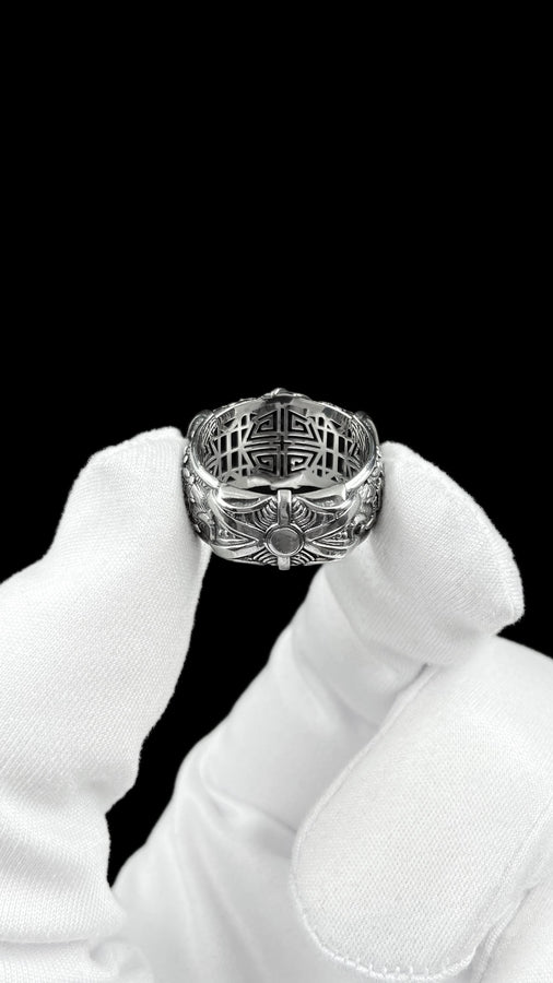 A close-up studio photograph of a wide sterling silver ring designed to look like folded fabric. The overlapping top mimics an Obi, the traditional Japanese kimono sash. The band features highly detailed relief carvings of Sakura (cherry blossoms) and Seigaiha (concentric ocean waves) patterns. A raised ribbon section bears engraved Japanese Kanji script. The silver is heavily oxidized in the recesses to highlight the intricate textures against t (etsy image id: 7831393878)