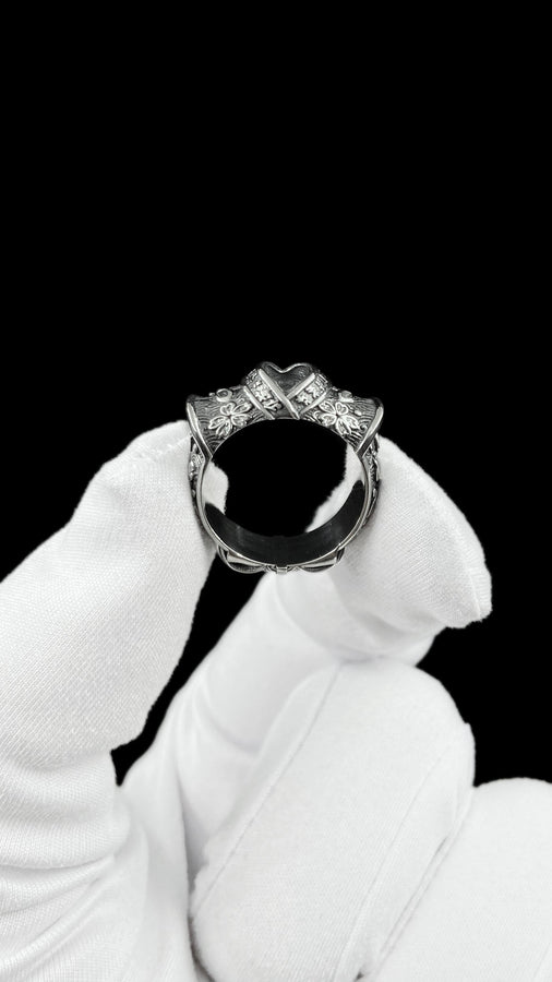 A close-up studio photograph of a wide sterling silver ring designed to look like folded fabric. The overlapping top mimics an Obi, the traditional Japanese kimono sash. The band features highly detailed relief carvings of Sakura (cherry blossoms) and Seigaiha (concentric ocean waves) patterns. A raised ribbon section bears engraved Japanese Kanji script. The silver is heavily oxidized in the recesses to highlight the intricate textures against t (etsy image id: 7831393878)