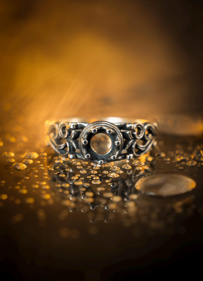 A macro studio shot of a sterling silver solitaire ring. The focal point is a round, clear gemstone (simulated diamond or white sapphire) held in a secure bezel setting. The band is composed of openwork filigree scrolls that swirl around the stone, creating a lace-like effect. The silver features a high-contrast finish: bright, polished vines against a matte black, oxidized background that adds depth and definition. (etsy image id: 7490069229)