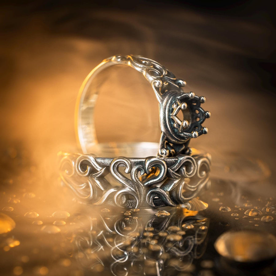 A macro studio shot of a sterling silver solitaire ring. The focal point is a round, clear gemstone (simulated diamond or white sapphire) held in a secure bezel setting. The band is composed of openwork filigree scrolls that swirl around the stone, creating a lace-like effect. The silver features a high-contrast finish: bright, polished vines against a matte black, oxidized background that adds depth and definition. (etsy image id: 7490069229)