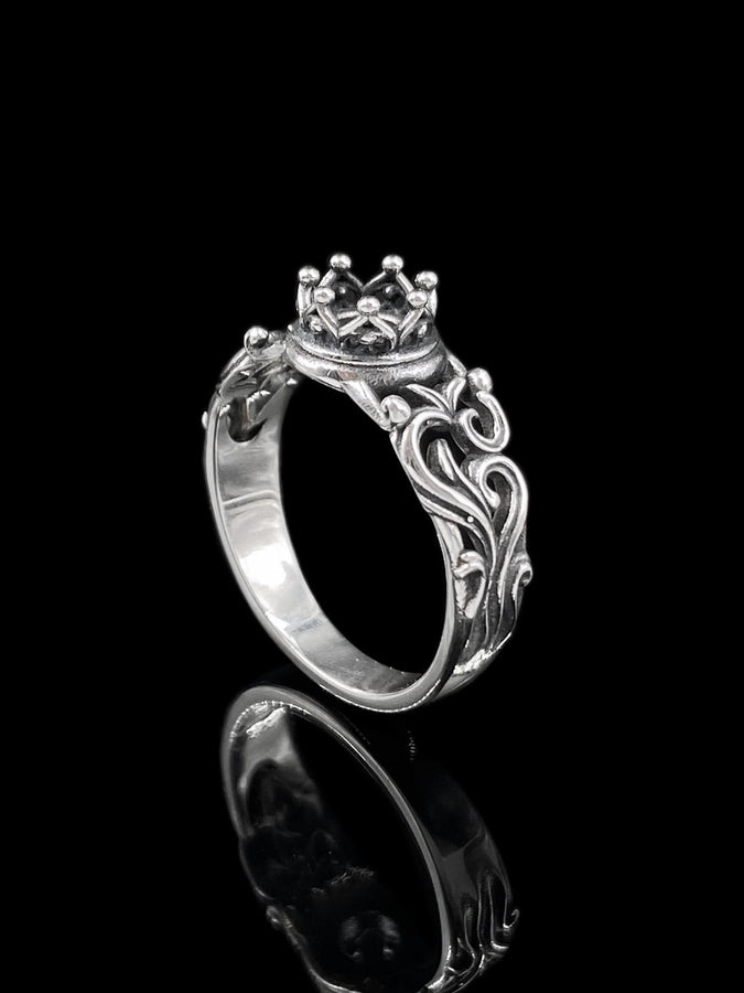 A macro studio shot of a sterling silver solitaire ring. The focal point is a round, clear gemstone (simulated diamond or white sapphire) held in a secure bezel setting. The band is composed of openwork filigree scrolls that swirl around the stone, creating a lace-like effect. The silver features a high-contrast finish: bright, polished vines against a matte black, oxidized background that adds depth and definition. (etsy image id: 7490069229)