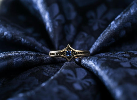 A macro shot of a vintage-inspired sterling silver ring. The focal point is a round, clear white gemstone set in a polished bezel. Flanking the center stone are two elongated, marquise-shaped sections on the band, each decorated with a row of small, pyramid-like silver studs. The background metal is heavily oxidized to a matte black, making the polished studs and the sparkling center stone stand out in high contrast. The ring rests on a dark, ref (etsy image id: 7433751958)