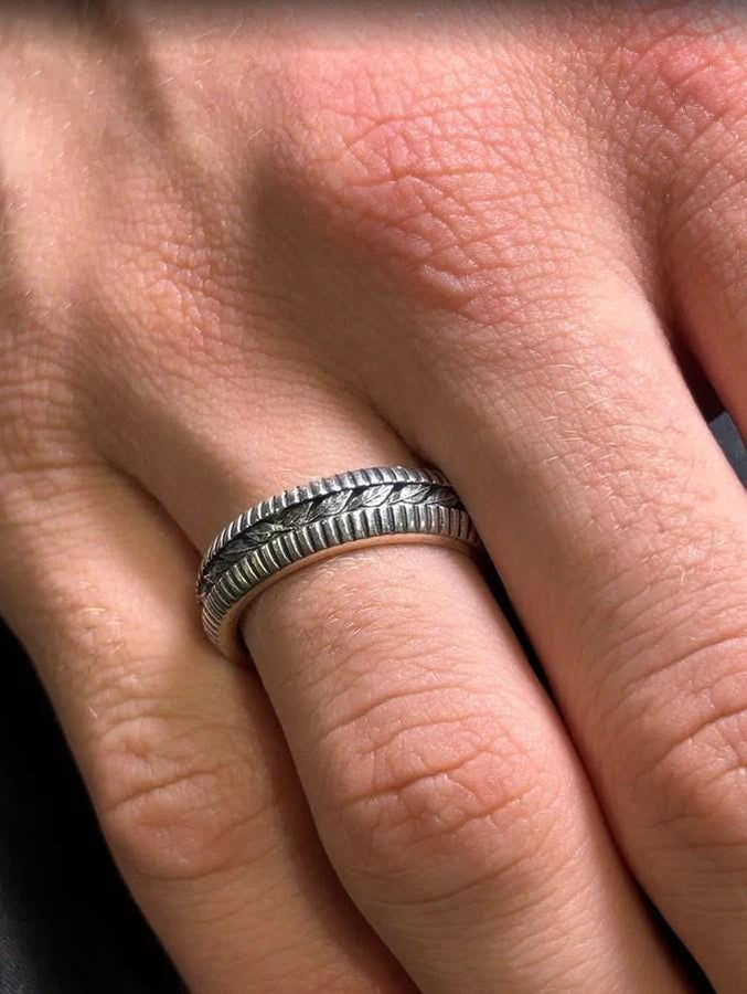 This sterling silver wedding band features intricate Victorian-inspired detailing, including finely engraved laurel leaves that wrap around the entire ring. The ribbed architectural edges create depth and texture, giving the piece an antique character reminiscent of handcrafted heirloom jewelry. Ideal for men or women who appreciate historic design and meaningful symbolism in their wedding band. __etsy:7473345891