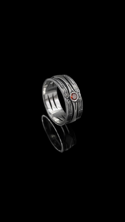 A high-contrast studio shot of a two-piece sterling silver ring set. The foreground features a wide band lying flat, set with a round clear gemstone. Flanking the stone are horizontal, grooved lines resembling arrows or spears. Standing behind it is a narrower engagement-style ring with a matching "lance-tip" shank leading to a central bezel-set white stone. The background is a textured, dark fabric. __etsy:7441122056