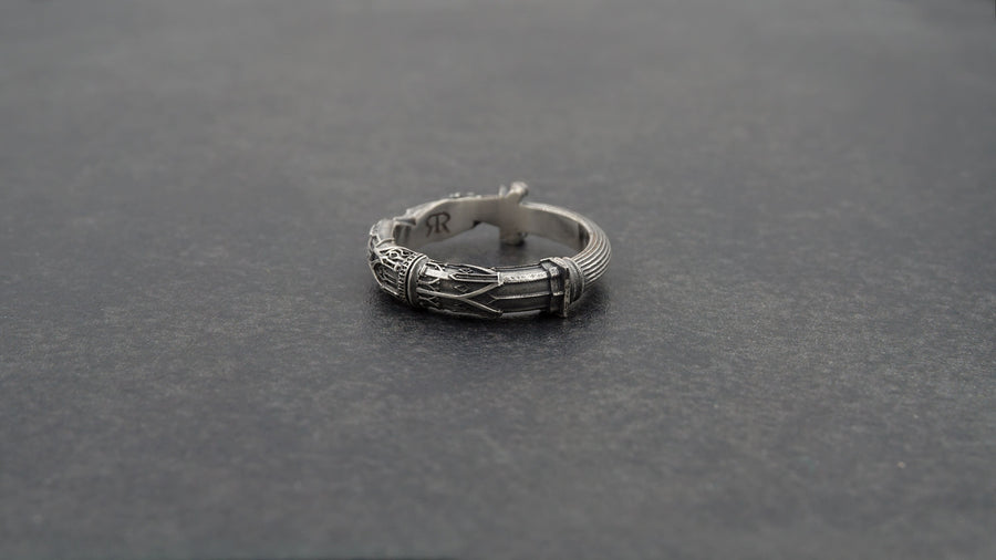 A cinematic studio shot of a sculptural sterling silver ring resting on a dark textured fabric. The focal point is two realistic hands clasped in a handshake (the Fede motif). Instead of fabric sleeves, the wrists emerge from architectural column capitals with distinct "volute" scrolls (Ionic style). The band continues as a textured, fluted column shaft. The silver is heavily oxidized to mimic ancient stone. (etsy image id: 7452415972)