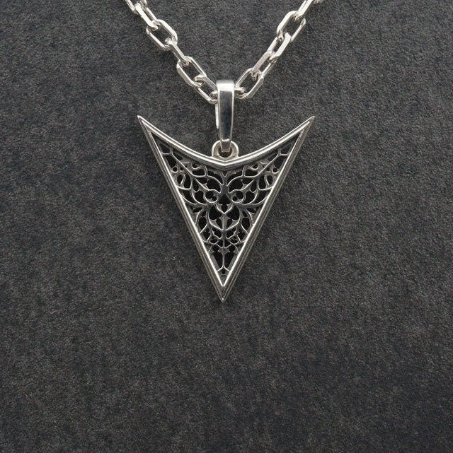 A detailed studio shot of an inverted triangle-shaped pendant hanging from a sturdy chain. The design features a "V" shape frame filled with complex, organic filigree. The inner pattern resembles branching roots, veins, or the "Flamboyant" style of late Gothic window tracery. The raised silver lines are polished bright, contrasting with the matte black oxidation in the negative spaces. (etsy image id: 7496362357)