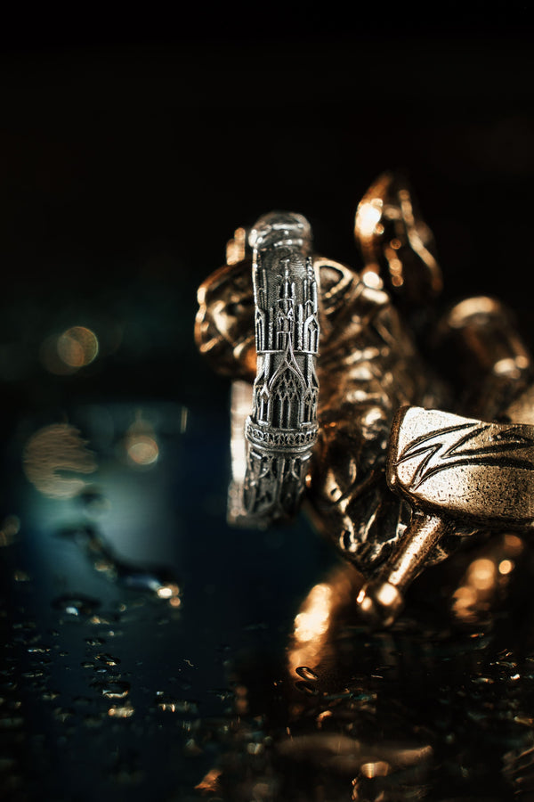 A cinematic studio shot of a sculptural sterling silver ring resting on a dark textured fabric. The focal point is two realistic hands clasped in a handshake (the Fede motif). Instead of fabric sleeves, the wrists emerge from architectural column capitals with distinct "volute" scrolls (Ionic style). The band continues as a textured, fluted column shaft. The silver is heavily oxidized to mimic ancient stone. (etsy image id: 7452415972)