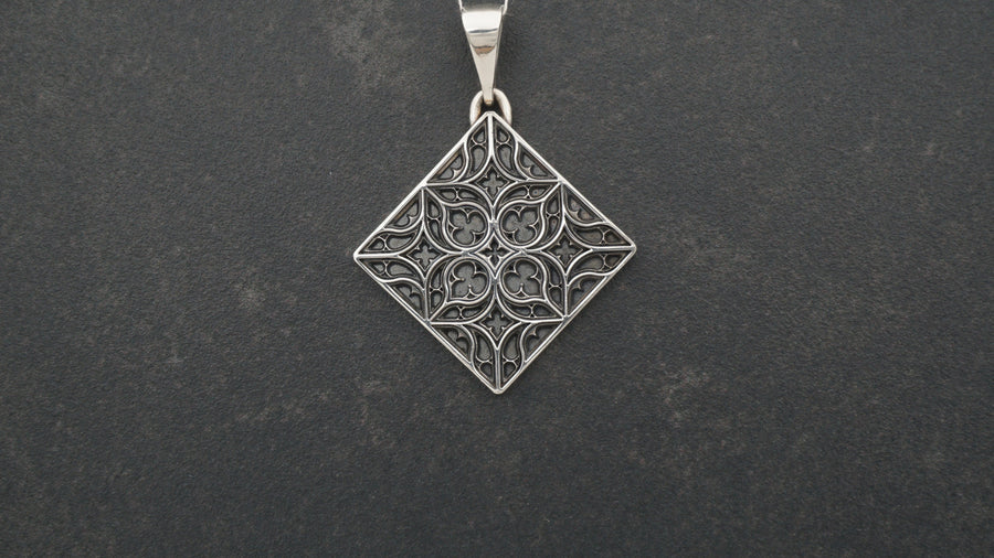 A detailed studio shot of a diamond-shaped (lozenge) sterling silver pendant hanging vertically. The design features intricate "curvilinear" Gothic tracery—four teardrop shapes meeting in the center to form a cross or quatrefoil. The raised lines are polished bright silver, while the negative space behind them is heavily oxidized to a matte black, creating a high-contrast architectural look. (etsy image id: 7494090955)