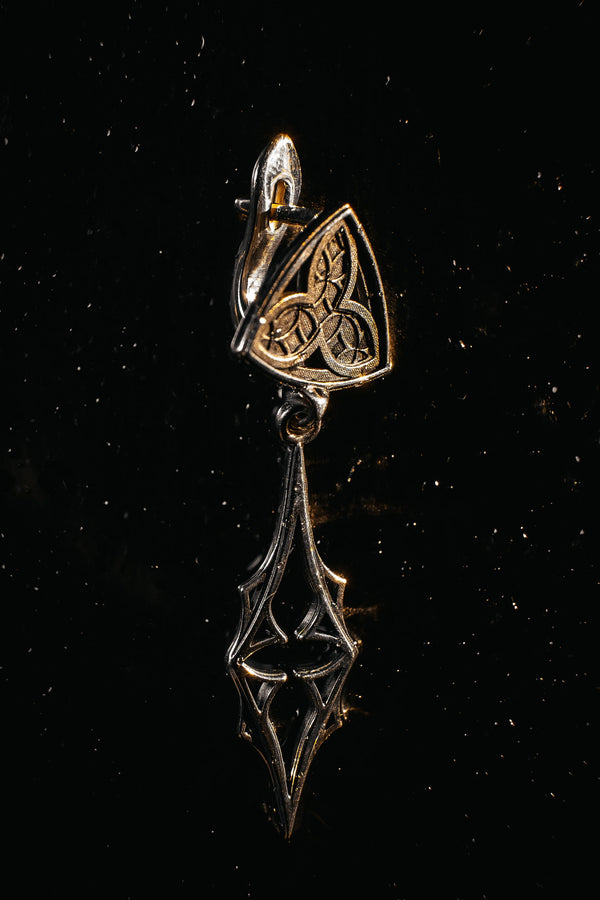 Embrace your dark beauty with our Gothic silver earrings. Unique design, premium silver, intricate details, and comfortable to wear.
A sharp studio shot of a pair of articulated silver earrings. The top stud is a soft triangle shape containing a raised "trefoil" or "trinity" knot pattern against a textured background. The bottom section is an elongated, openwork drop that tapers to a sharp point, resembling a Gothic spire or a (etsy image id: 7218877462)