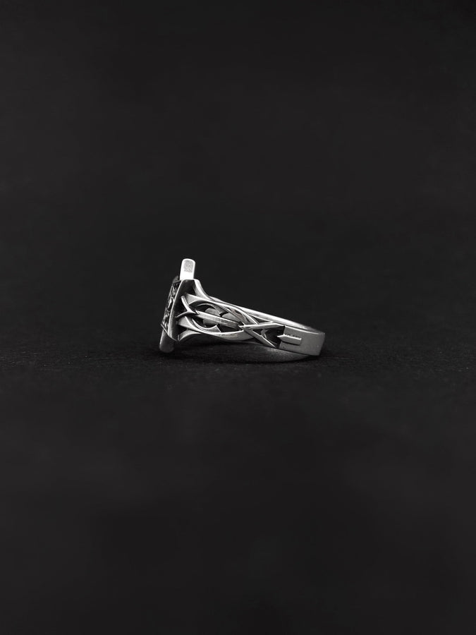 A detailed studio shot of a sterling silver ring held in a gloved hand. The focal point is a geometric "North Star" face—a square frame turned on its point, embellished with top and bottom spikes. Inside the frame is a floral quatrefoil pattern surrounding a round, bezel-set white gemstone (Diamond or CZ). The silver is polished on the raised lines and dark in the recesses. (etsy image id: 7452221522)