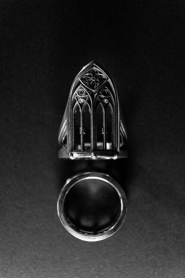A clean studio shot of a tall, architectural sterling silver ring standing on a matte grey surface. The ring creates the silhouette of a Gothic "Lancet Window." It features three vertical openings separated by slender bars (mullions), topped by an intricate geometric tracery design within the pointed arch. The metal is matte silver with dark oxidation in the corners. (etsy image id: 7500328125)