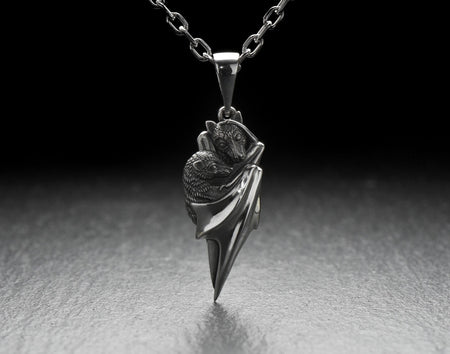 A detailed close-up studio shot of a sterling silver pendant shaped like two flying foxes or fruit bats. The bats are intimately huddled together, wrapped within the smooth, sweeping folds of their leathery wings. The metal is highly textured to show the fine details of their fur and faces. The silver is heavily oxidized in the recesses, creating a striking contrast against the polished highlights of the wings. (etsy image id: 5592925539)