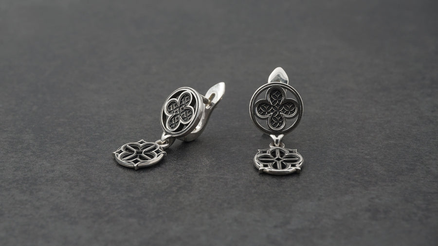 The image highlights the specific textures of the casting. The top stud has a "waffle" or lattice texture inside the quatrefoil lobes, mimicking chainmail or stone carving. The bottom drop is smooth and open, providing a visual counterweight. The 925 sterling silver is treated with an antique patina to enhance the "old world" feel. Modeled as a versatile daily earring, the "coin" size is modest enough for office wear (etsy image id: 5775868859)