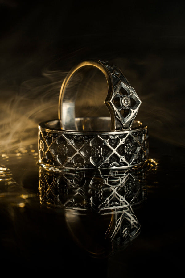 A professional studio photograph of a matching two-piece sterling silver wedding ring set. Both rings feature a prominent, raised Greek-style cross motif in the center, which holds a round, bezel-set white crystal. The interior of the cross arms has a fine, cross-hatched grid texture. Along the sides of the high-polished silver bands are recessed, four-lobed quatrefoil shapes. The rings are presented against a pitch-black background, making the p __etsy:8051335185