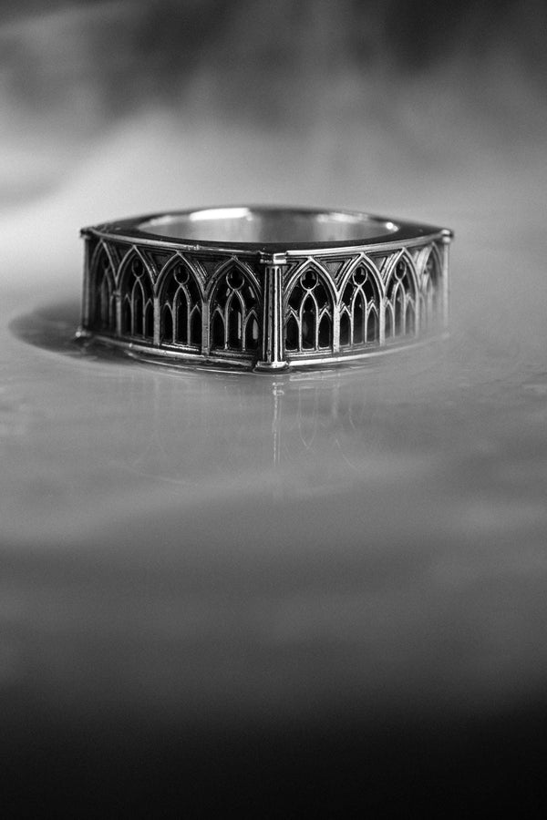 Defend your realm with this architectural fortress ring. Distinctive for its soft-square outer profile, this sterling silver band features a continuous cloister of Gothic arches anchored by robust corner buttresses. The geometric design mimics the stone ramparts of a medieval castle. Heavily oxidized to reveal the depth of the masonry, it is a symbol of unshakeable strength and structure. A bold statement for the guardian of history. (etsy image id: 7450412634)