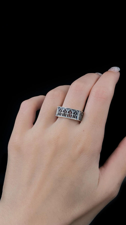 Defend your realm with this architectural fortress ring. Distinctive for its soft-square outer profile, this sterling silver band features a continuous cloister of Gothic arches anchored by robust corner buttresses. The geometric design mimics the stone ramparts of a medieval castle. Heavily oxidized to reveal the depth of the masonry, it is a symbol of unshakeable strength and structure. A bold statement for the guardian of history. (etsy image id: 7450412634)