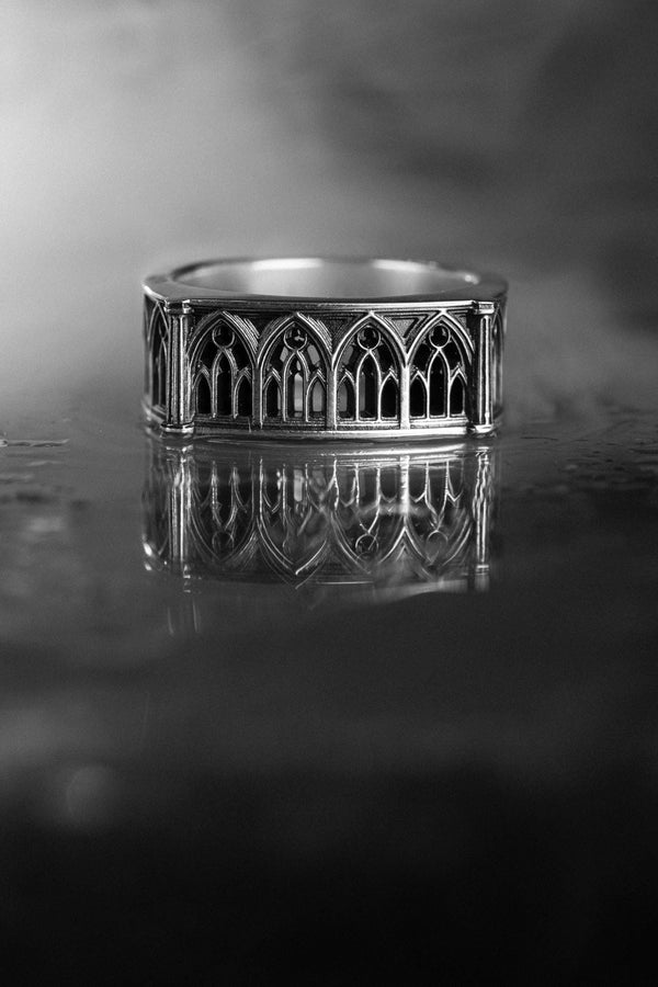 Defend your realm with this architectural fortress ring. Distinctive for its soft-square outer profile, this sterling silver band features a continuous cloister of Gothic arches anchored by robust corner buttresses. The geometric design mimics the stone ramparts of a medieval castle. Heavily oxidized to reveal the depth of the masonry, it is a symbol of unshakeable strength and structure. A bold statement for the guardian of history. (etsy image id: 7450412634)