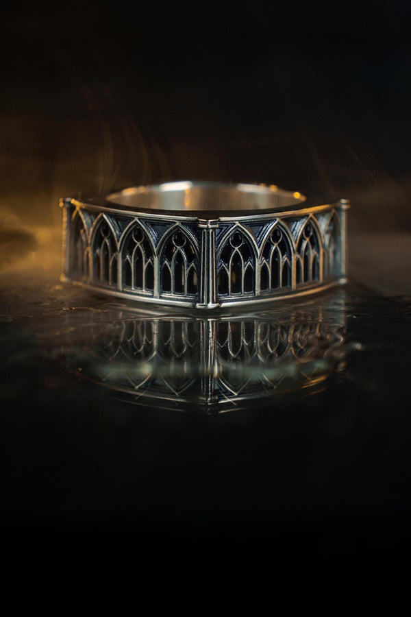 Defend your realm with this architectural fortress ring. Distinctive for its soft-square outer profile, this sterling silver band features a continuous cloister of Gothic arches anchored by robust corner buttresses. The geometric design mimics the stone ramparts of a medieval castle. Heavily oxidized to reveal the depth of the masonry, it is a symbol of unshakeable strength and structure. A bold statement for the guardian of history. (etsy image id: 7450412634)