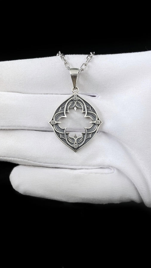 Sterling Silver Gothic Pendant, Holiday Gift, Handmade Medieval Pendant, Goth Necklace, Gothic Jewelry, A cinematic studio shot of a diamond-shaped sterling silver pendant hanging against a smoky, amber-lit background. The design is "openwork," featuring a central cutout in the shape of a four-lobed quatrefoil with sharp, barbed cusps. The silver frame mimics the stone mullions of a Gothic window. The metal is polished on the ridges and (etsy image id: 6258009905)