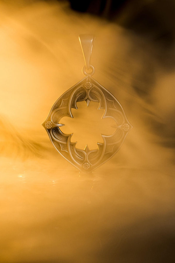 Sterling Silver Gothic Pendant, Holiday Gift, Handmade Medieval Pendant, Goth Necklace, Gothic Jewelry, A cinematic studio shot of a diamond-shaped sterling silver pendant hanging against a smoky, amber-lit background. The design is "openwork," featuring a central cutout in the shape of a four-lobed quatrefoil with sharp, barbed cusps. The silver frame mimics the stone mullions of a Gothic window. The metal is polished on the ridges and (etsy image id: 6258009905)
