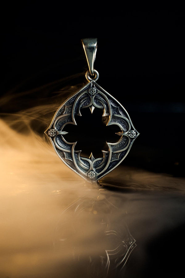 Sterling Silver Gothic Pendant, Holiday Gift, Handmade Medieval Pendant, Goth Necklace, Gothic Jewelry, A cinematic studio shot of a diamond-shaped sterling silver pendant hanging against a smoky, amber-lit background. The design is "openwork," featuring a central cutout in the shape of a four-lobed quatrefoil with sharp, barbed cusps. The silver frame mimics the stone mullions of a Gothic window. The metal is polished on the ridges and (etsy image id: 6258009905)