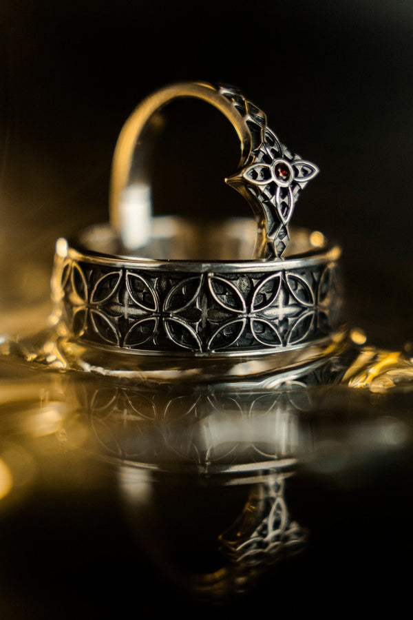 A professional studio photograph of a matching two-piece sterling silver wedding ring set. Both rings feature a prominent, raised Greek-style cross motif in the center, which holds a round, bezel-set white crystal. The interior of the cross arms has a fine, cross-hatched grid texture. Along the sides of the high-polished silver bands are recessed, four-lobed quatrefoil shapes. The rings are presented against a pitch-black background, making the p __etsy:8051335185