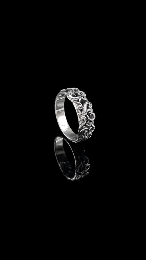 A high-contrast studio shot of a two-piece sterling silver ring set. The top ring features a raised, three-dimensional "crown" or "coronet" motif with small spheres on the tips. The bottom ring is a matching wide band. Both rings are covered in intricate, raised scrollwork or vine-like filigree. The silver is polished bright on the raised swirls, contrasting with the black oxidized background.