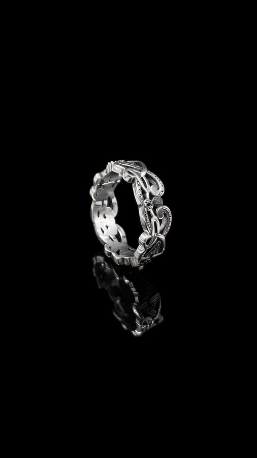 A studio shot of a matching two-piece sterling silver ring set on a black reflective surface. The standing ring is a signet style featuring an oval face with a raised Triskelion (triple spiral) motif. The ring lying flat is a wide band with an "openwork" or cut-out Celtic knot pattern. The silver is highly polished on the raised surfaces, contrasting with the dark shadows of the open areas.