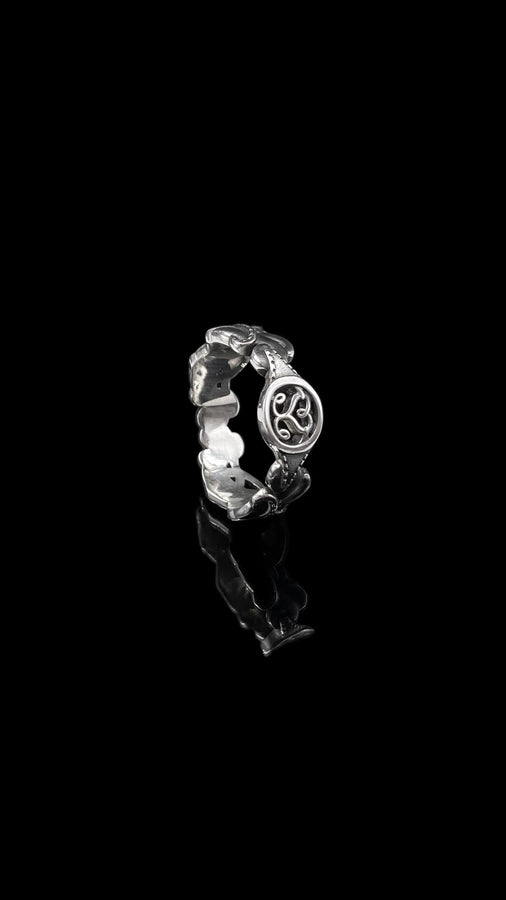 A studio shot of a matching two-piece sterling silver ring set on a black reflective surface. The standing ring is a signet style featuring an oval face with a raised Triskelion (triple spiral) motif. The ring lying flat is a wide band with an "openwork" or cut-out Celtic knot pattern. The silver is highly polished on the raised surfaces, contrasting with the dark shadows of the open areas.