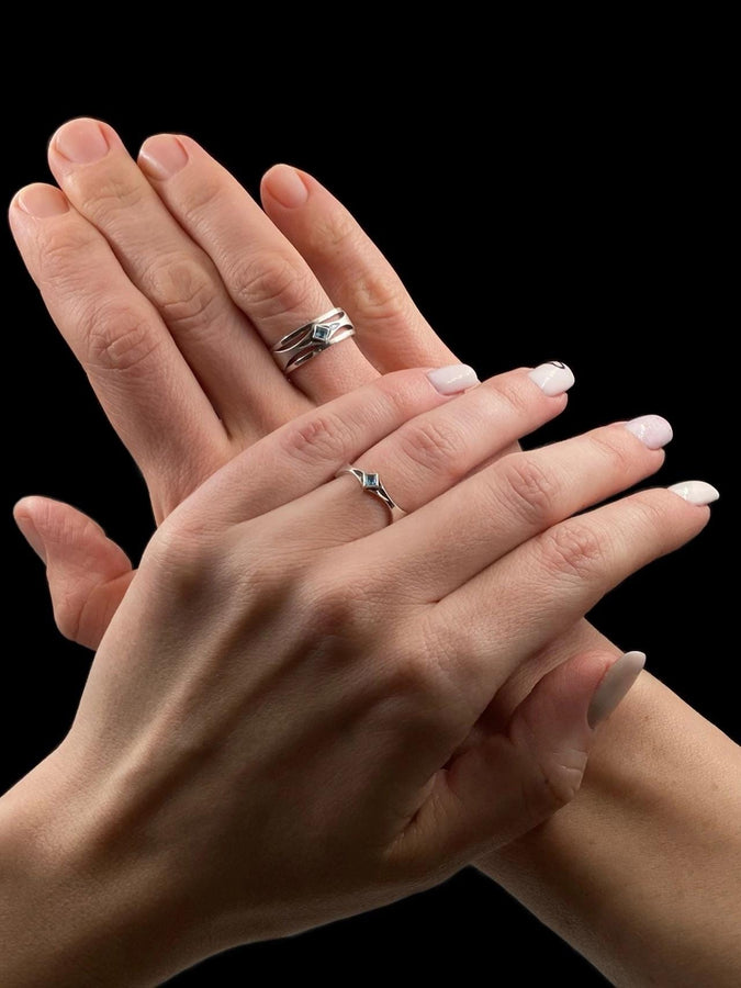This Art Deco wedding ring set features a sterling silver engagement ring and matching band with bold geometric cutouts and a bright blue square gemstone. The clean lines, layered shapes, and sculptural silhouette create a modern yet vintage feel ideal for couples seeking unique, architecturally inspired bridal jewelry captured on a reflective surface for elegant presentation.