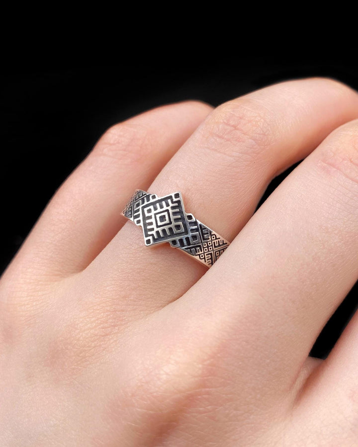A studio shot of a two-piece sterling silver ring set with a high-contrast black and silver finish. The standing ring features a square, diamond-shaped face created by stepped geometric lines. The lying ring is a wide band with a continuous "zig-zag" or "step" pattern running around the circumference. The design mimics the look of cross-stitch embroidery or pixelated ancient art rendered in metal.