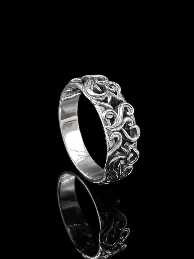 A high-contrast studio shot of a two-piece sterling silver ring set. The top ring features a raised, three-dimensional "crown" or "coronet" motif with small spheres on the tips. The bottom ring is a matching wide band. Both rings are covered in intricate, raised scrollwork or vine-like filigree. The silver is polished bright on the raised swirls, contrasting with the black oxidized background.